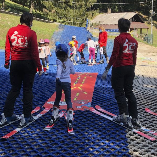 alcuni istruttori mentre insegnano ai ragazzini a sciare sulla pista diplastica
